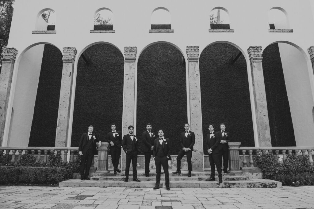 Groom and groomsmen standing in front of waterfall wall, bell tower on 34th